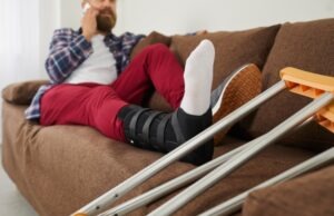 A on a couch with a leg brace and crutches speaking on the phone with a Temple City pedestrian accident lawyer.